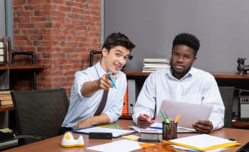 front view work process two businessmen sitting desk one them pointing with finger camera