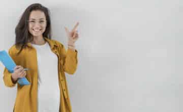smiley pregnant woman holding clipboard pointing up with copy space