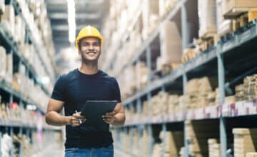 smart indian engineer man wearing safety helmet doing stock tick check cardboard stock product management factory warehouse background