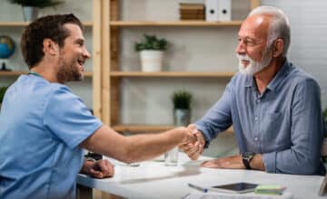 happy doctor greeting handshaking with senior patient his office focus is senior man