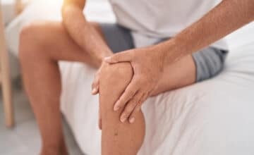 young blond man suffering knee injury sitting bed bedroom