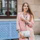 cool young beautiful stylish woman walking street pink coat holding purse hands listening music